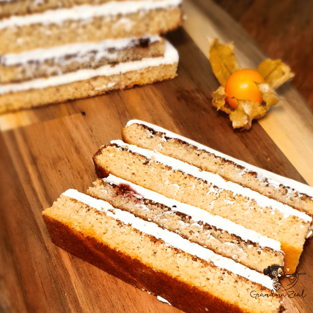 A slice of low-carb honey cake on a wooden board, with the rest of the cake in the background and a piece of fruit beside it
