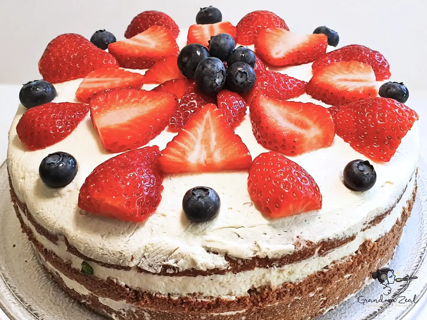 Easy vanilla sponge cake topped with mascarpone frosting, decorated with blueberries and sliced strawberries