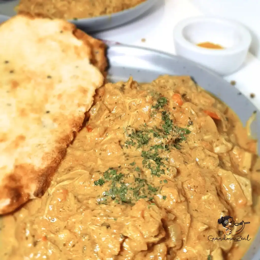 Chicken-aubergine curry with low-carb Indian-style bread, a small bowl of spices, and a second plate blurred in the background