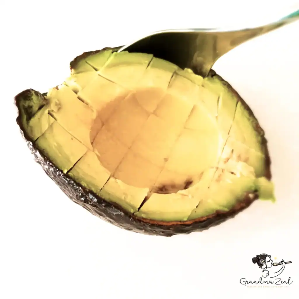 Close-up of a halved avocado in its skin, flesh scored into squares with a spoon inserted to demonstrate how easily the pieces lift out.