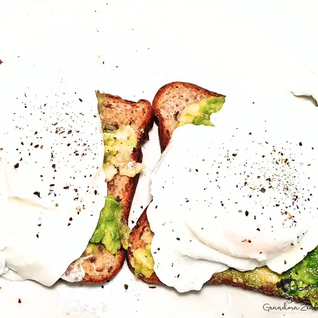 Two slices of toast topped with mashed avocado and poached eggs, finished with freshly ground black pepper.