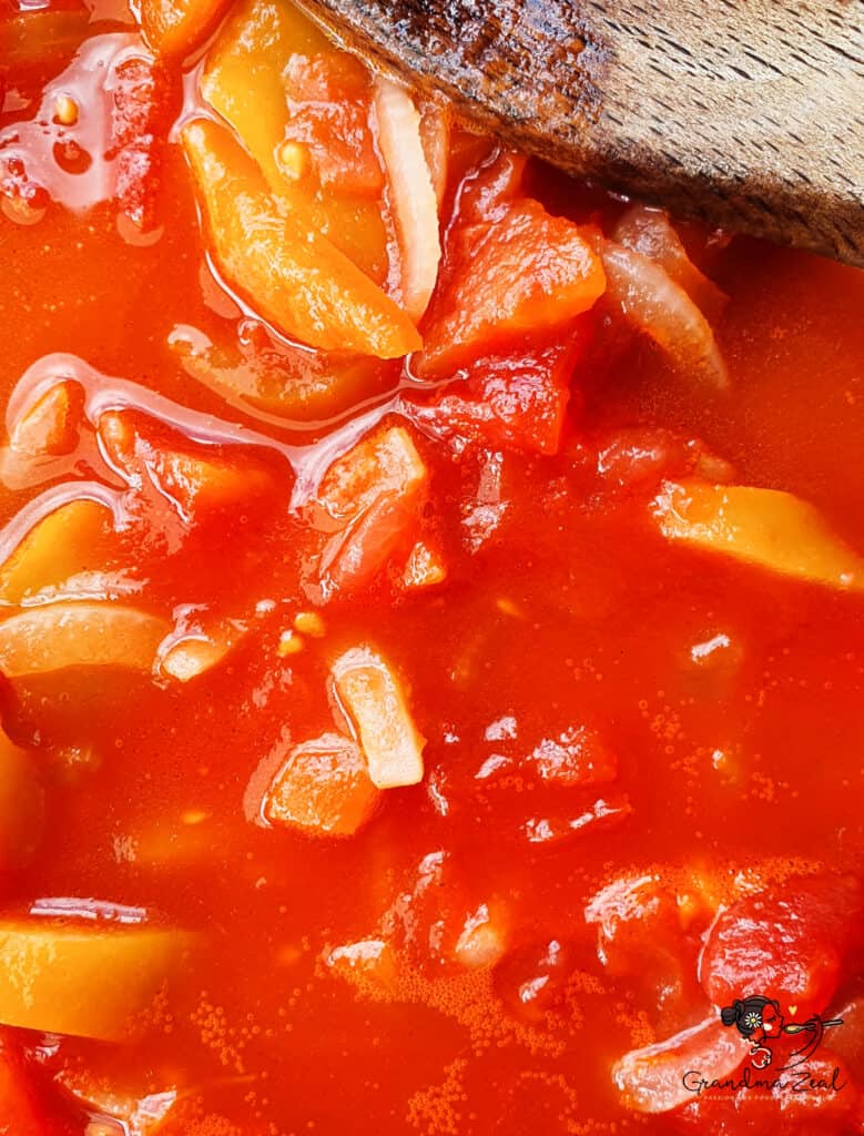 Chopped tomatoes and sliced peppers cooking with onions in a pan for lecso