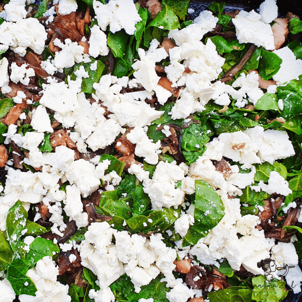 Bacon, vegetables, chopped spinach, and crumbled feta layered in a baking tray as the base for a crustless quiche.