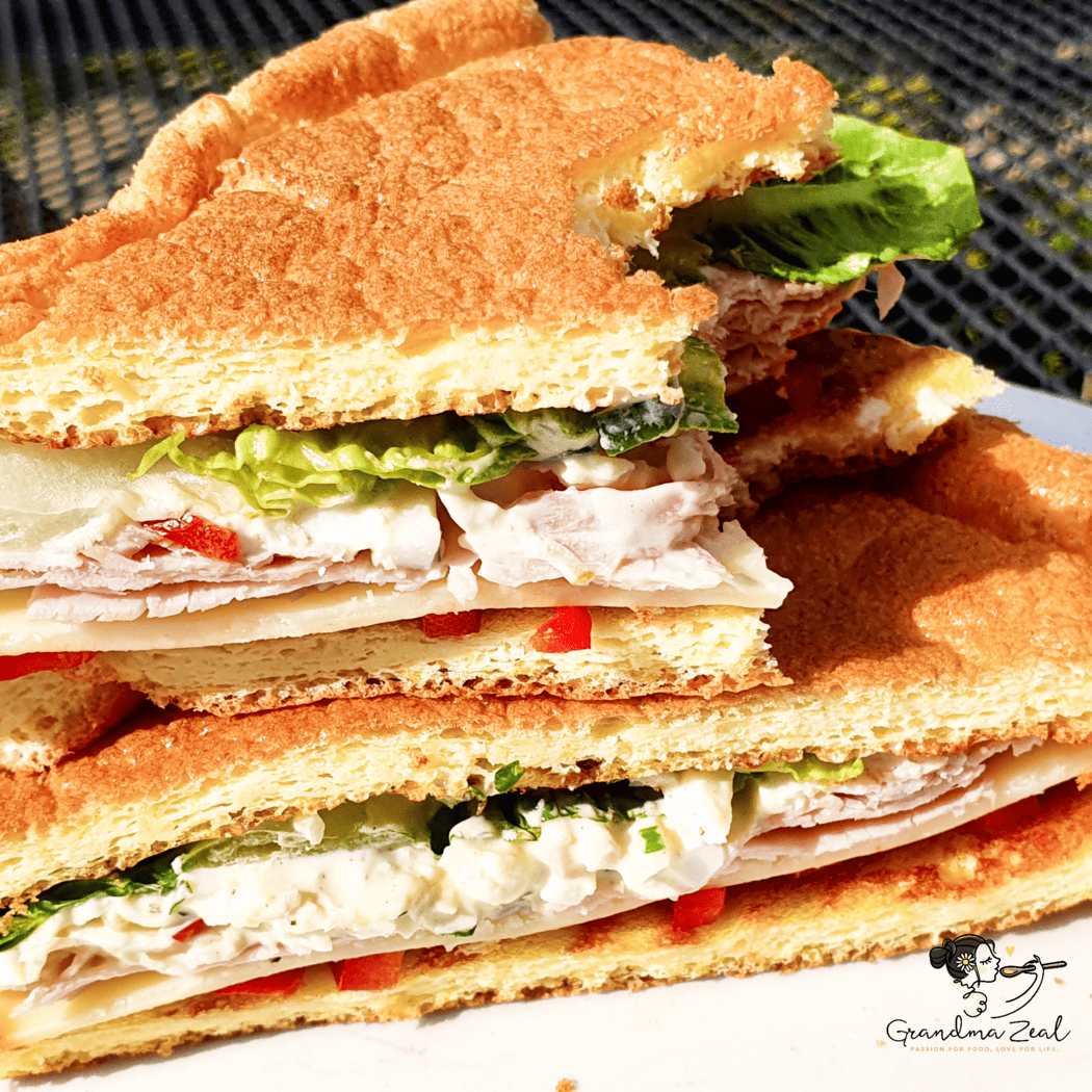 Close-up of a keto cloud bread sandwich with a bite taken out of the top triangle, filled with egg mayo, lettuce and ham.