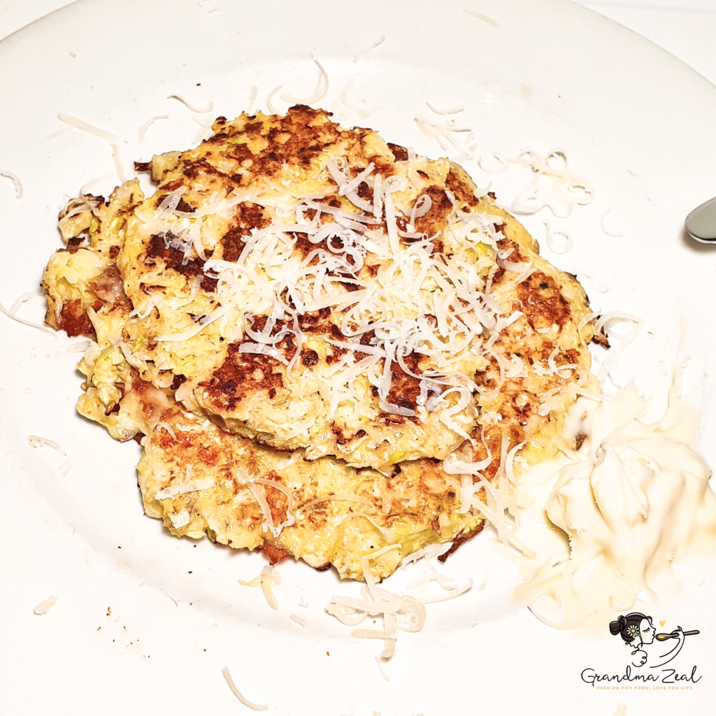 Two cabbage hash browns on a plate topped with a sprinkle of grated cheese