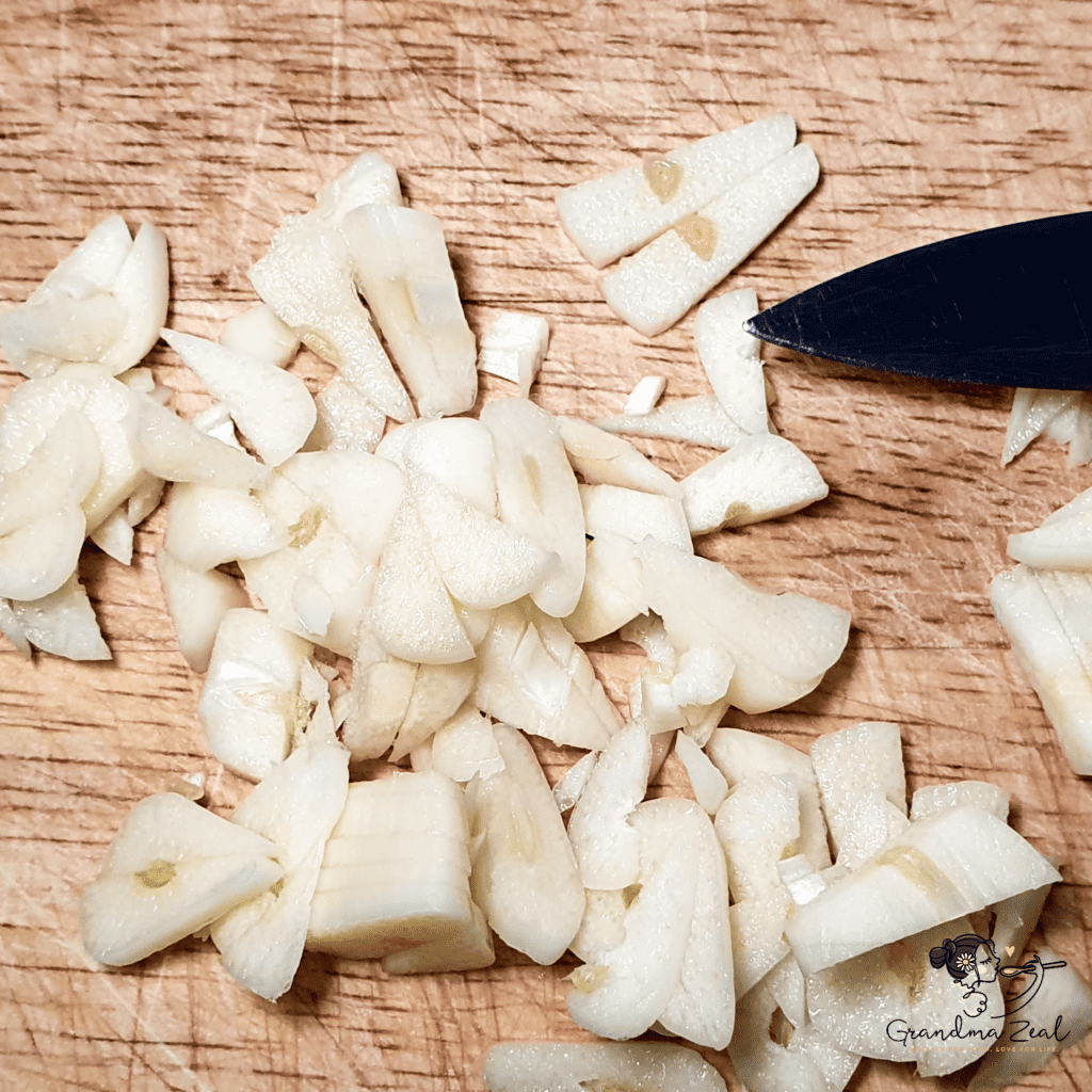 Chopped garlic on a wooden chopping board, ready to be added to the dish.