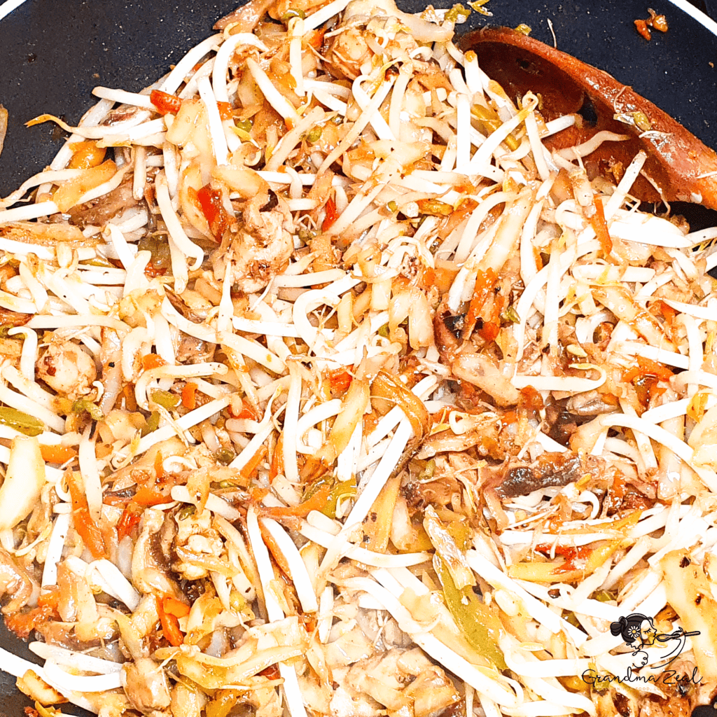 Bean sprouts added to cooked chicken chow mein in the pan