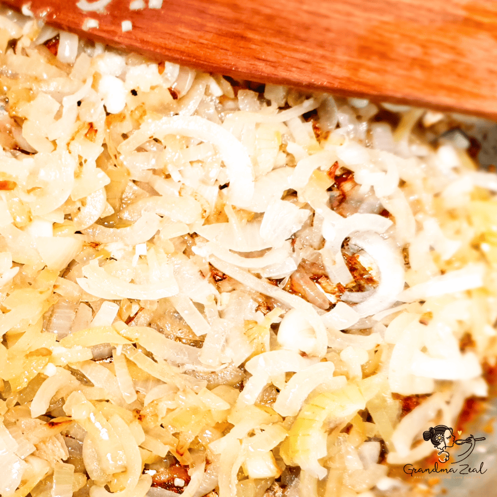 Close-up of sliced onion being sautéed for chicken-aubergine curry