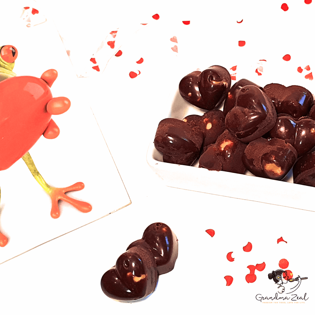 Little chocolate hearts with hazelnuts arranged in a white box next to a Valentine’s card