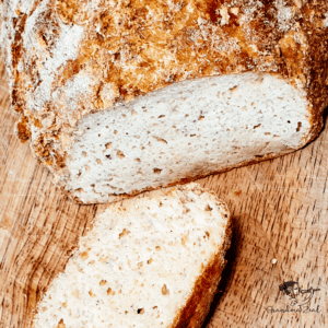 A slice and loaf of homemade keto rye bread on a wooden chopping board, showing its crusty texture and hearty crumb.