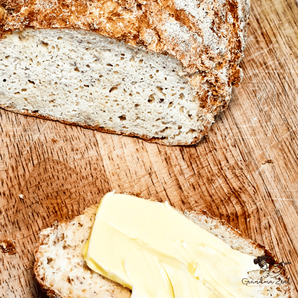 A slice of keto rye bread with butter next to the whole loaf on a wooden chopping board.