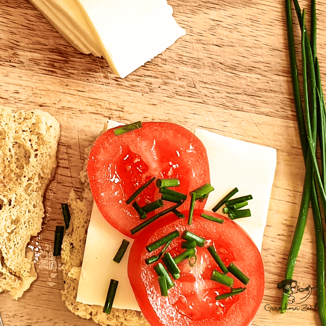 Close-up of a slice of 90-second microwave bread topped with butter, mozzarella, sliced tomatoes, and chives