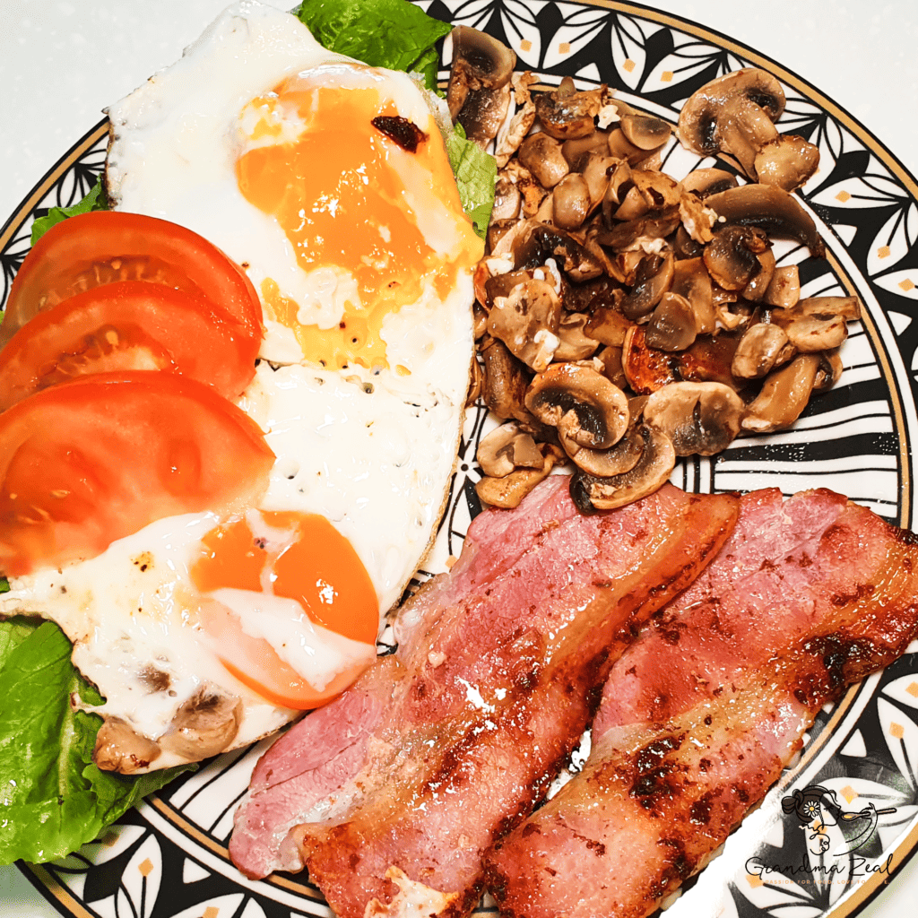 A portion of English breakfast with a twist – bacon, mushrooms, fried eggs, and sliced tomatoes on a plate
