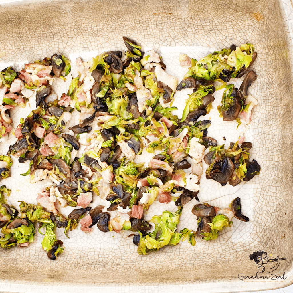 Fried bacon, courgette, and mushrooms layered in a baking tray, ready for the crustless quiche.