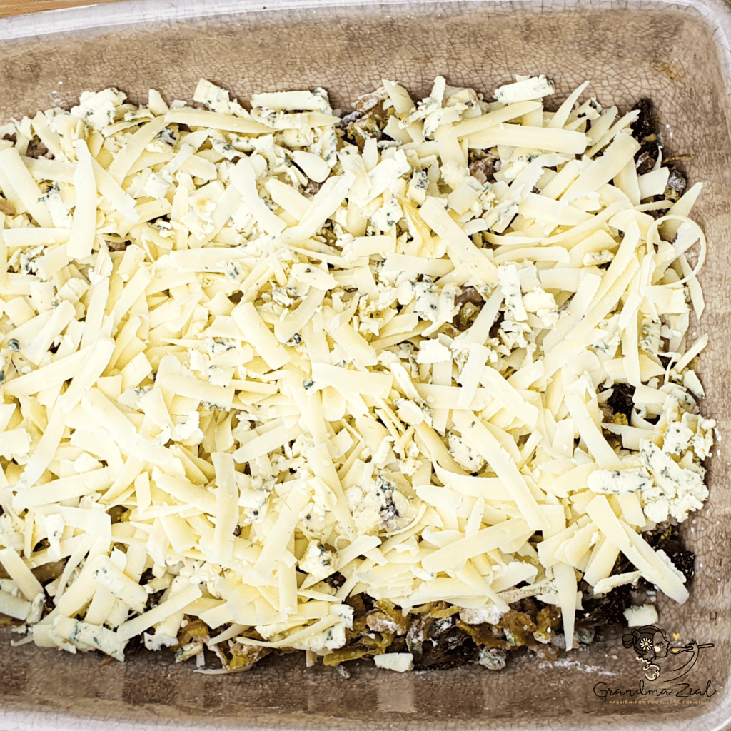 Fried bacon, courgette, mushrooms, and onion mixed with potato fibre and topped with grated cheese in a baking tray for crustless quiche.
