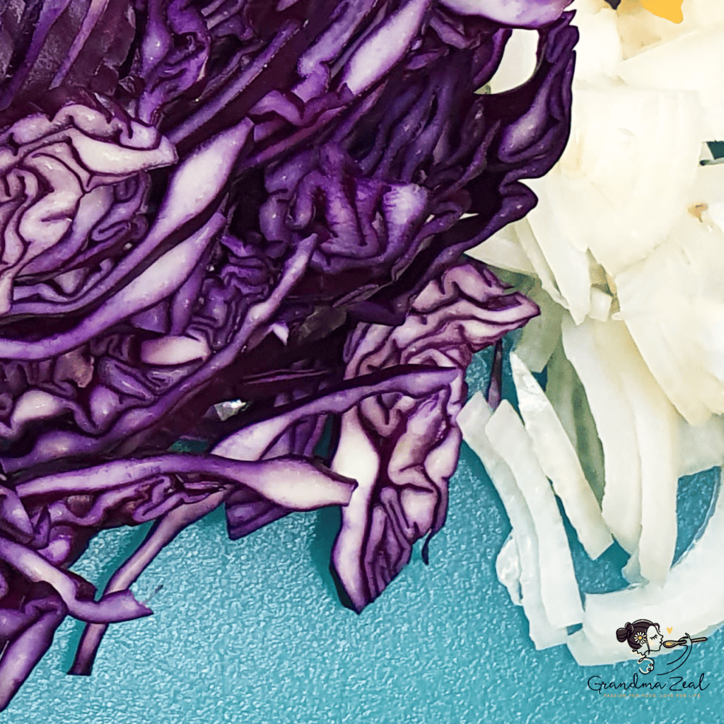 Sliced red cabbage and onion on a chopping board, ready for coleslaw
