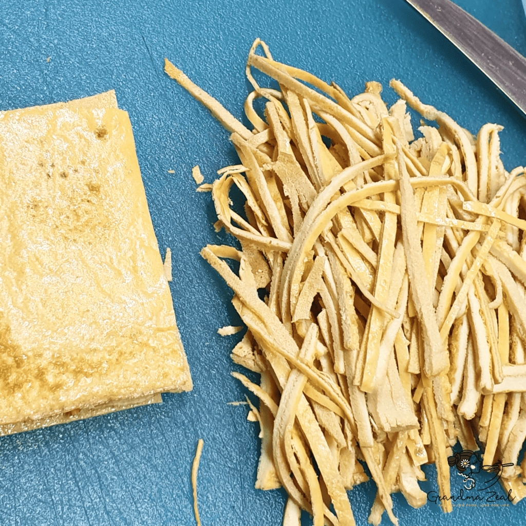 Low-carb high-fibre pasta being cut into strips on a wooden chopping board, ready for cooking.