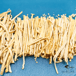 Thinly sliced homemade high-fibre pasta noodles on a wooden chopping board, ready to use in low-carb meals.