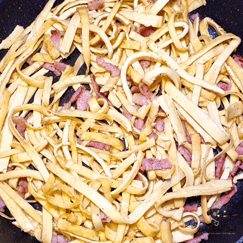 EASY HOMEMADE LOW-CARB TAGLIATELLE WITH QUARK CHEESE AND BACON Heating low-carb tagliatelle with bacon in the frying pan.
