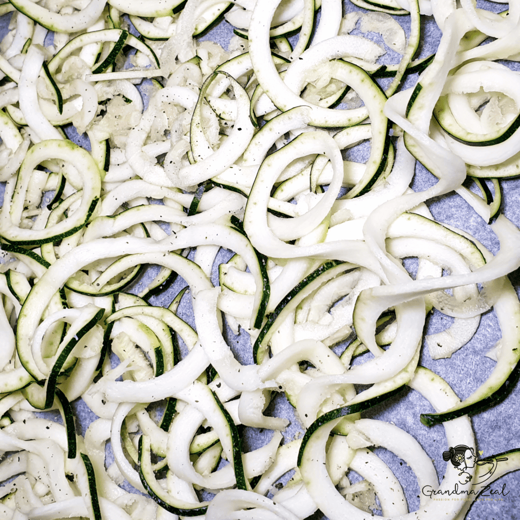 Courgette zoodles spread on a baking tray lined with parchment paper, ready to bake.