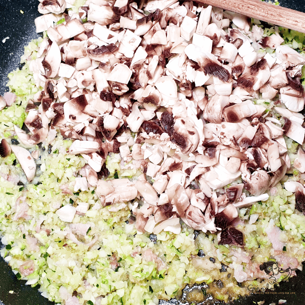 Chopped mushrooms, courgette, and garlic in a frying pan, sizzling in butter as the base for a healthy carbonara sauce.