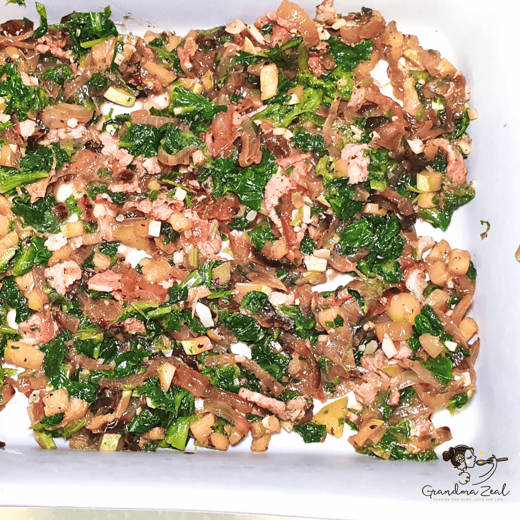 Cooked bacon and vegetables arranged in a baking tray, forming the base of a crustless quiche before adding the egg mixture.