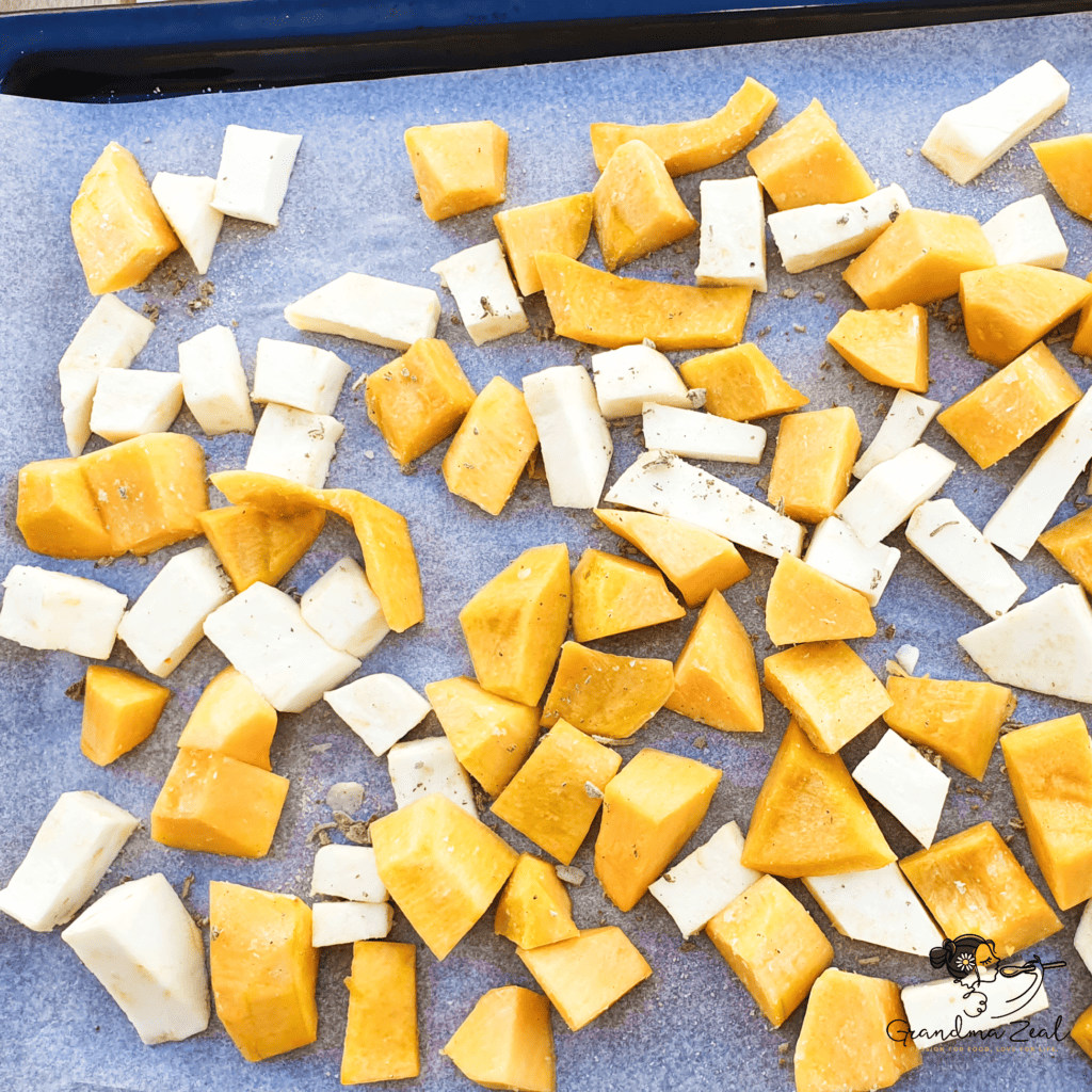 Cubed squash and root vegetables spread on a baking tray, seasoned and ready to roast.