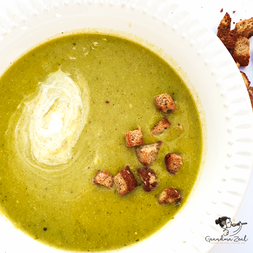 Healthy green vegetable soup with cheese served in a white plate, topped with sour cream and croutons