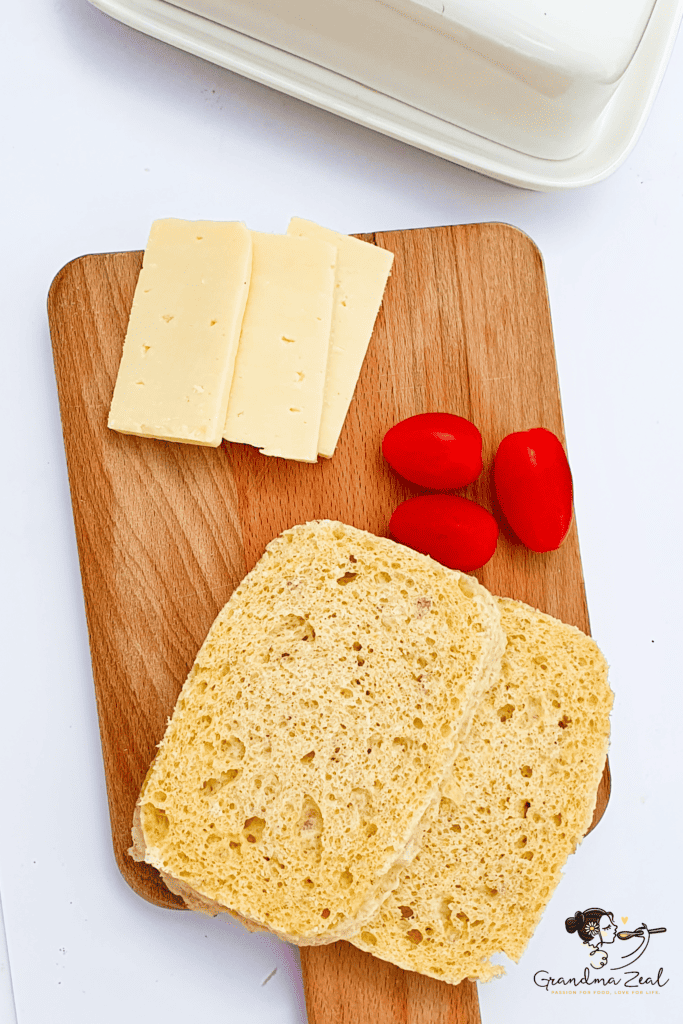 Two slices of 90-second microwave bread on a wooden board with cheese slices and mini tomatoes