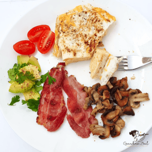 Low-carb breakfast with microwave bread, fried egg, bacon, avocado slices, mushrooms, and cherry tomatoes on a plate