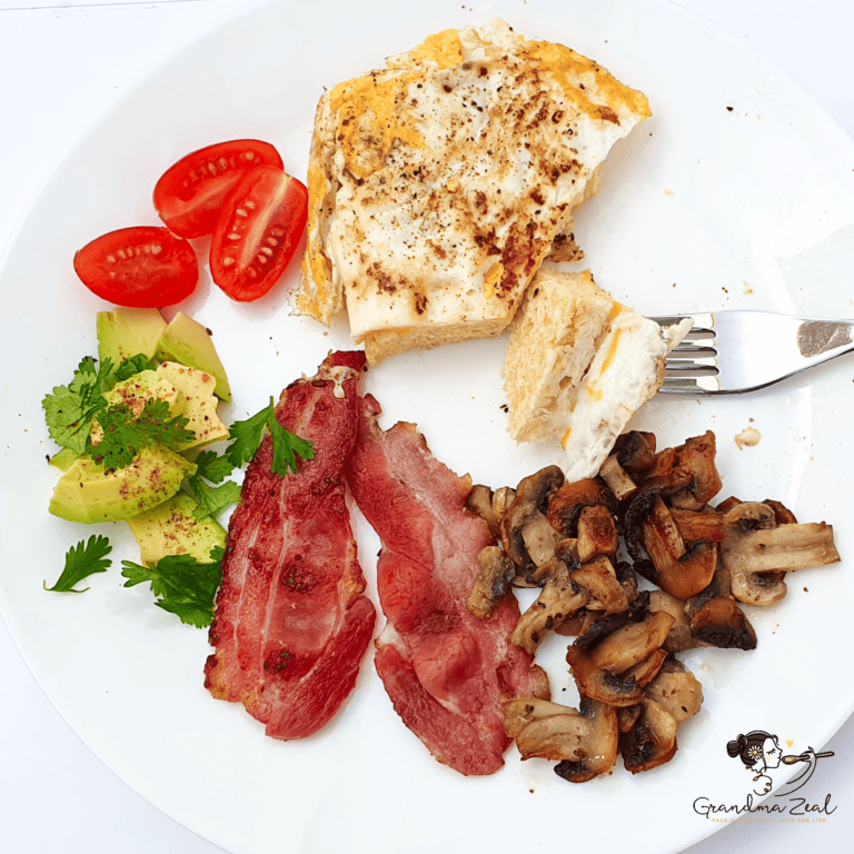 Low-carb breakfast with microwave bread, fried egg, bacon, avocado slices, mushrooms, and cherry tomatoes on a plate