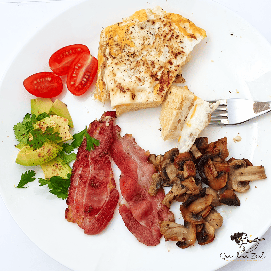 Low-carb breakfast with microwave bread, fried egg, bacon, avocado slices, mushrooms, and cherry tomatoes on a plate