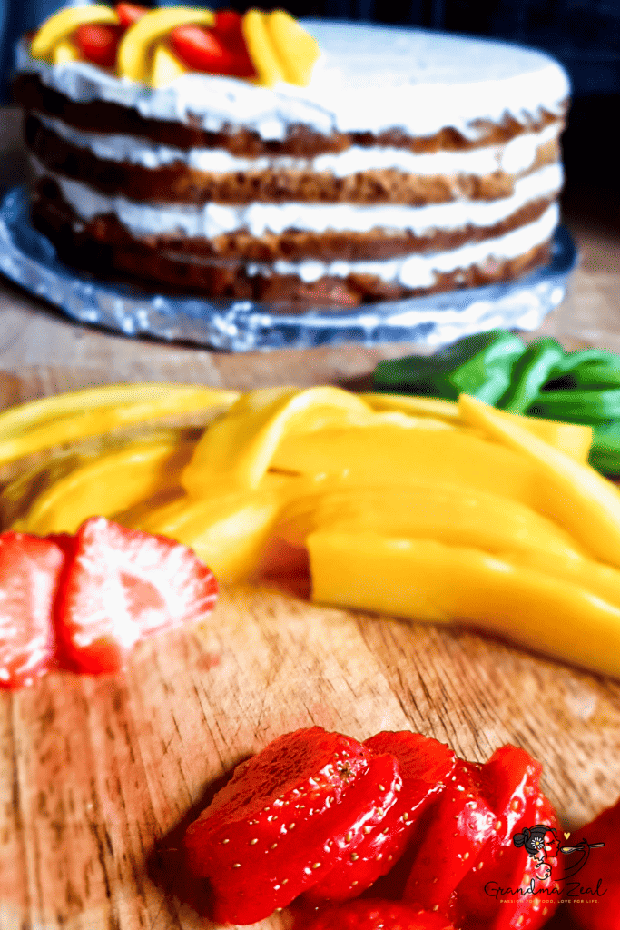 Strawberry and mango on a wooden board with a four-layer low-carb birthday honey cake in the background