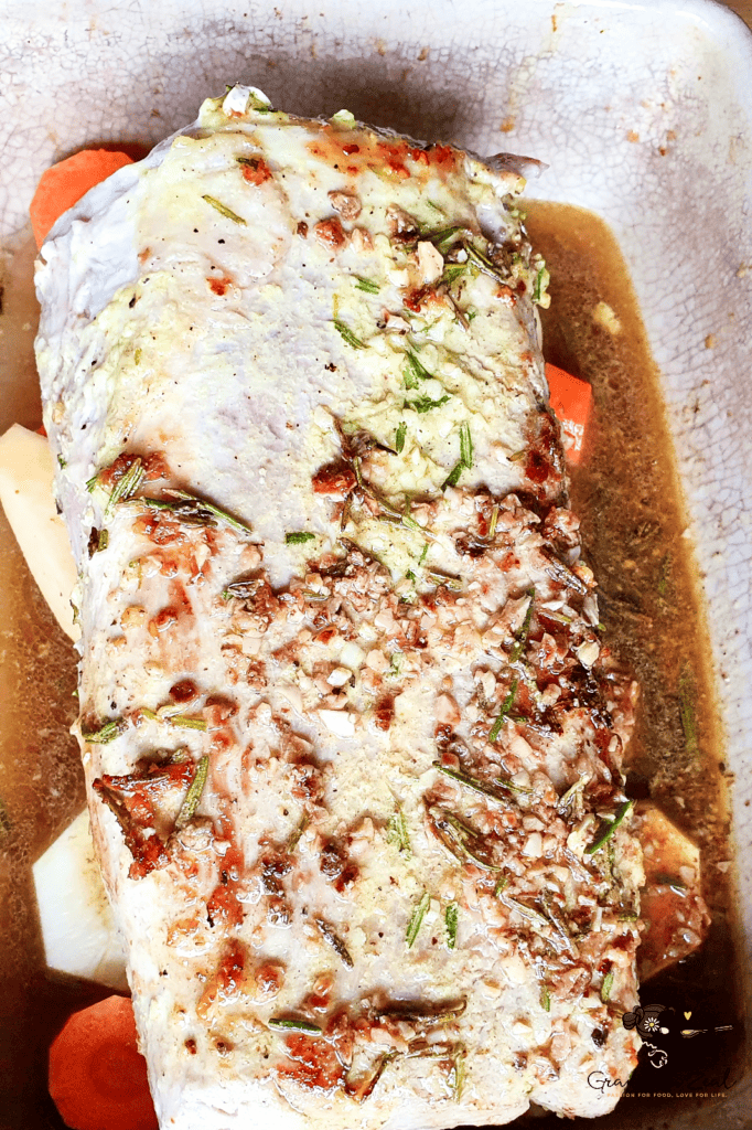 Seared pork loin placed on top of chopped root vegetables in a roasting tray, ready for the oven
