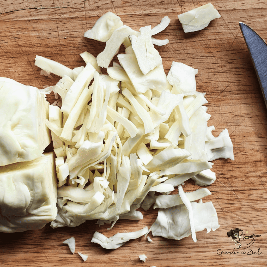 Cabbage being shredded on a wooden chopping board.