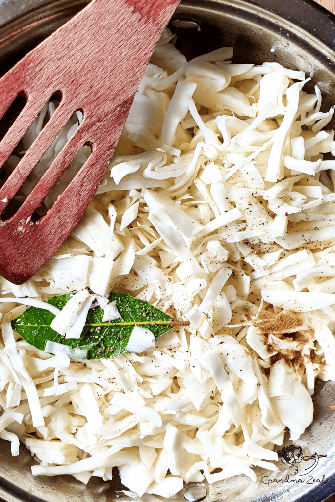Shredded cabbage in a wide pot with added spices on top, ready to cook.