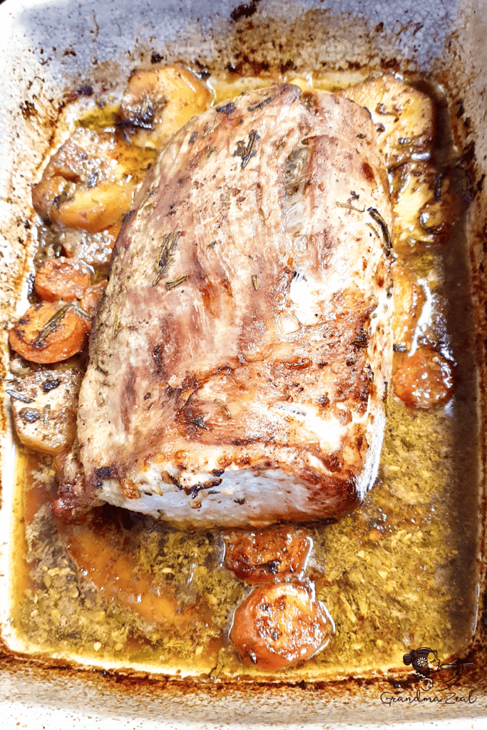 Roasted pork loin in a tray surrounded by vegetables and cooking juices