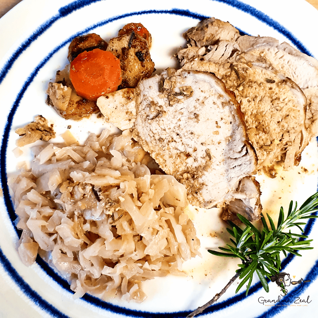 A plate of rosemary and garlic pork loin served with sautéed cabbage, roast vegetables, stuffing, and a sprig of rosemary