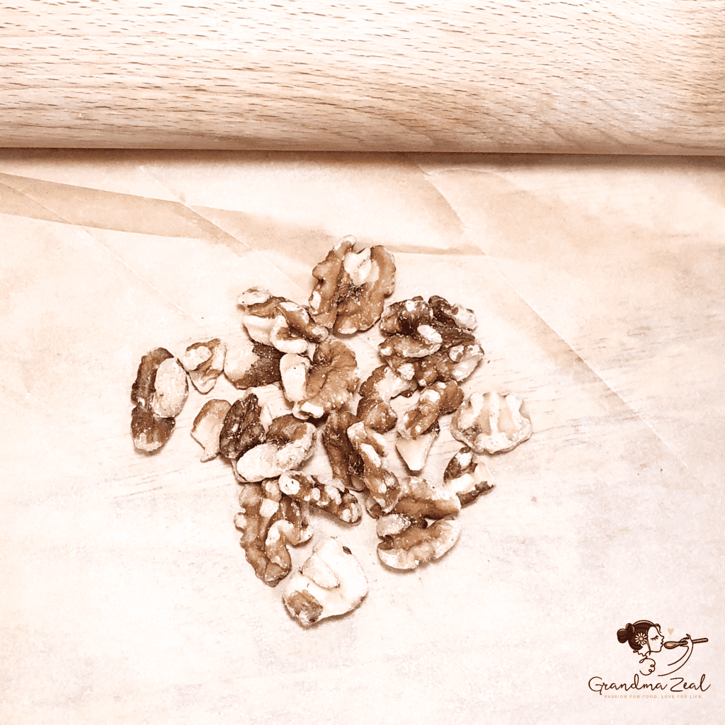 Walnuts being crushed with a rolling pin on a wooden board