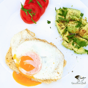 Single fried egg on a slice of 90-second low-carb bread, served with chopped seasoned avocado and sliced tomato on the side