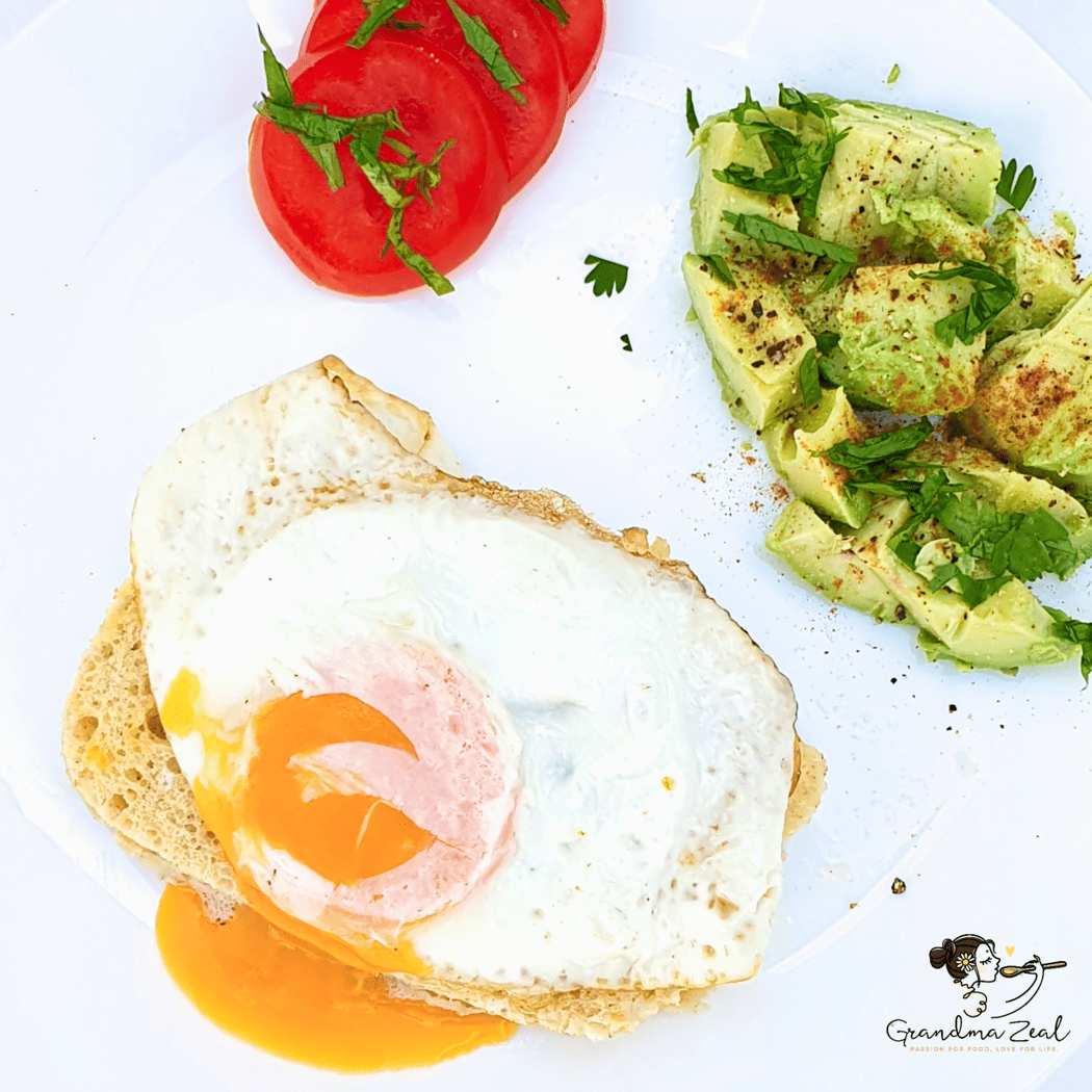 Single fried egg on a slice of 90-second low-carb bread, served with chopped seasoned avocado and sliced tomato on the side
