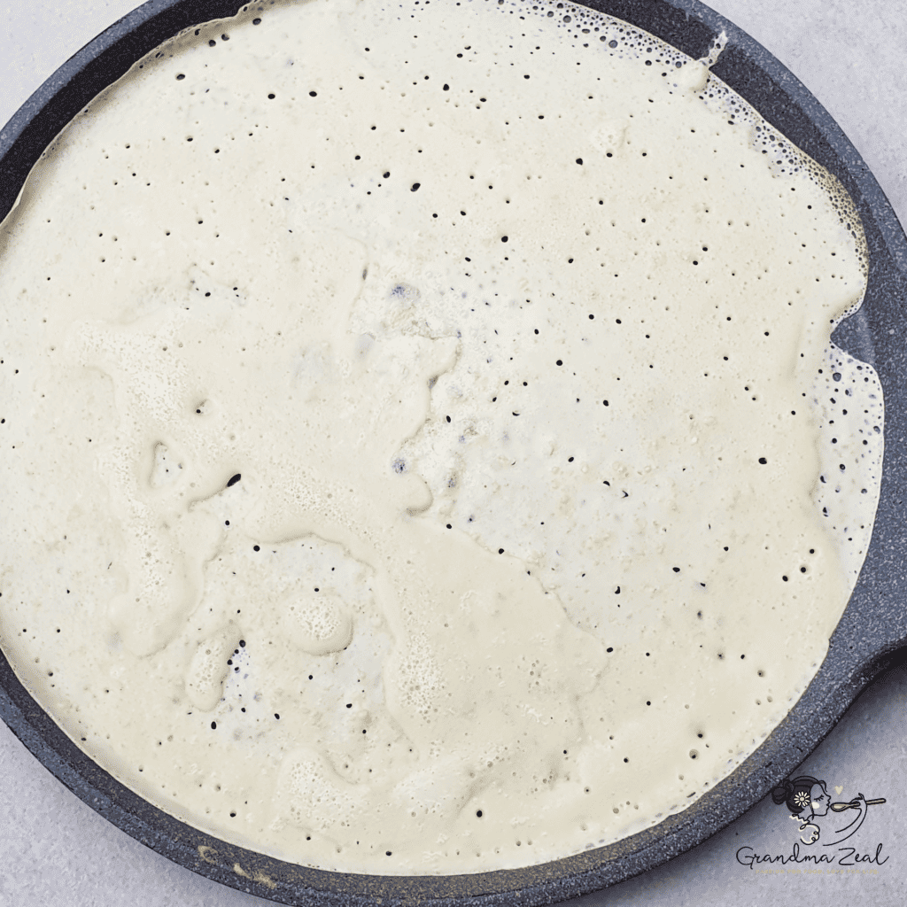 Crepe batter cooking on a non-stick pan, step in the process of making classic crepes