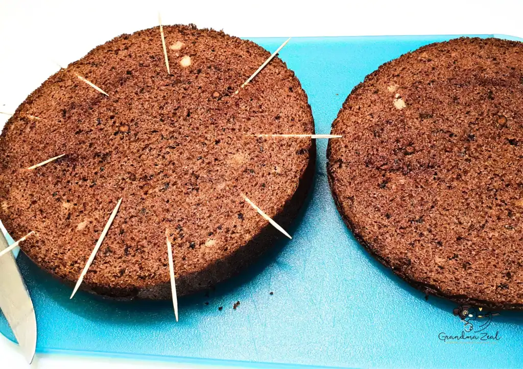 Chocolate sponge cake layers with toothpicks used as a cutting guide on a blue board