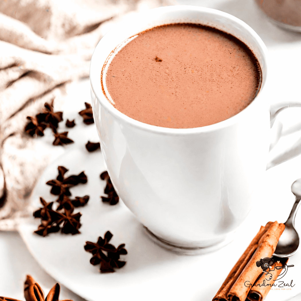Hot chocolate in a mug decorated with a cinnamon stick, with chocolate clusters on the saucer