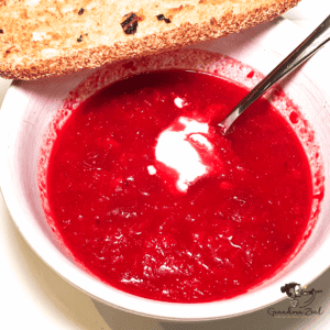 Bowl of beetroot soup served with a slice of garlic bread on the side