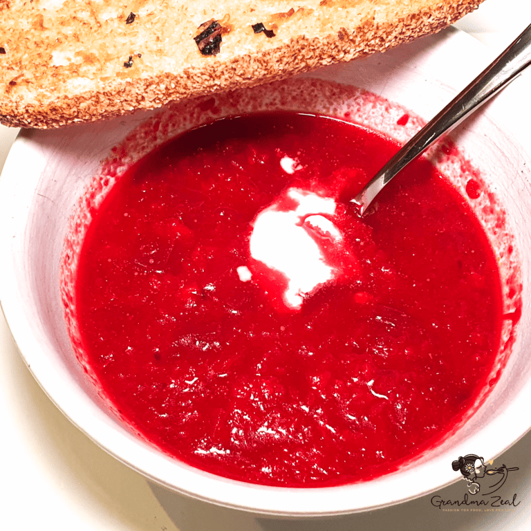 Bowl of beetroot soup served with a slice of garlic bread on the side