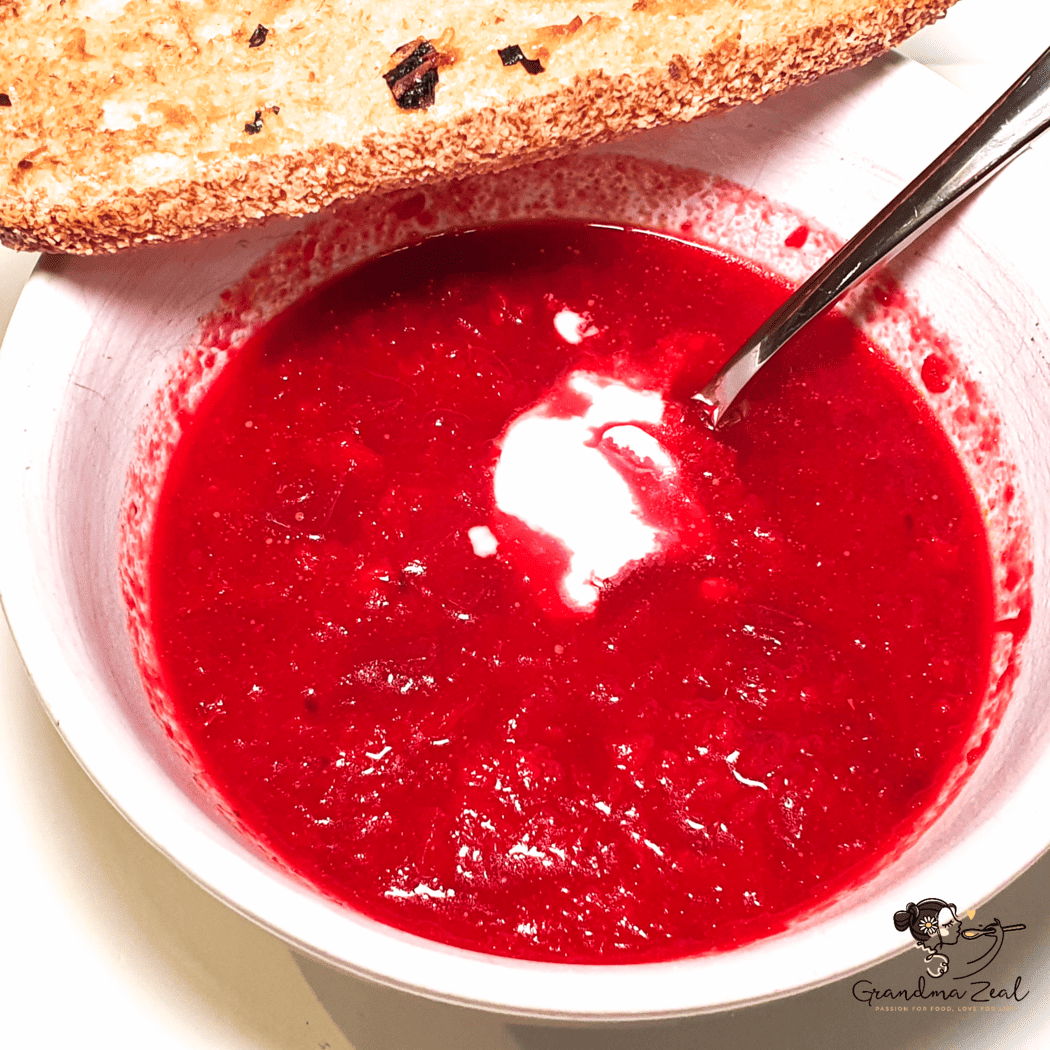 Bowl of beetroot soup served with a slice of garlic bread on the side