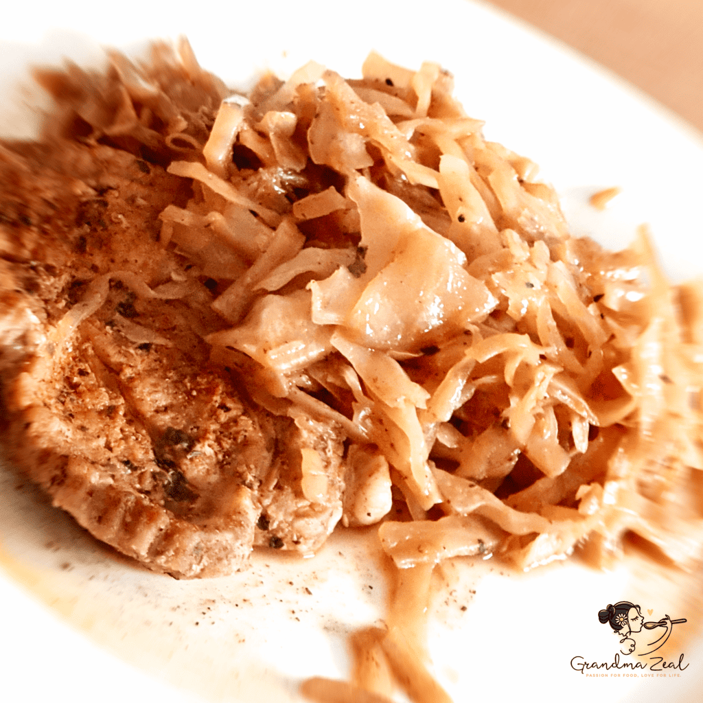 Close-up image of sautéed cabbage served with a slice of roast pork.