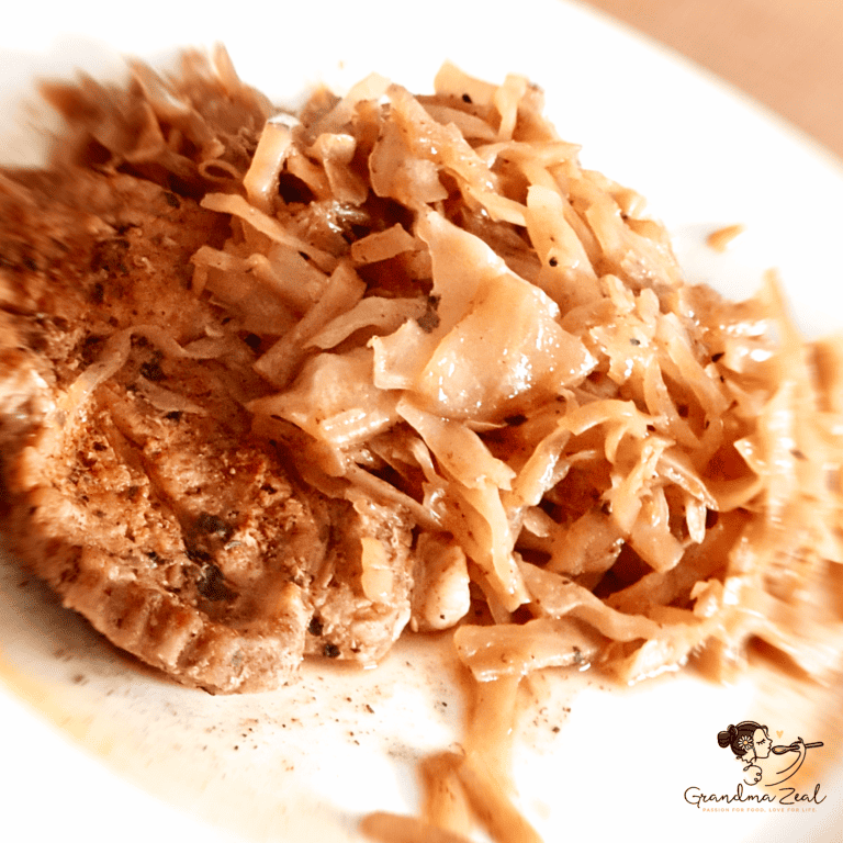 Close-up image of sautéed cabbage served with a slice of roast pork.