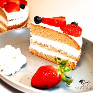 Slice of easy vanilla sponge cake with mascarpone frosting, served with extra frosting and a fresh strawberry on the side